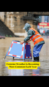 Emergency personnel in a high viz jacket wades through flooding to place a warning sign in the middle of the road, indicating climate breakdown and its impact on property insurance premiums