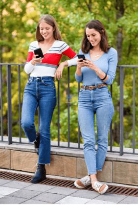 Two Gen Z Women stand outdoors while they check their bankig app on their mobile phones