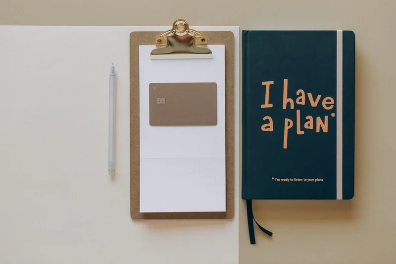 How to Create a Budget for Beginners: Aerial view of a desk with clipboard and notebook entitled 'I have a plan'