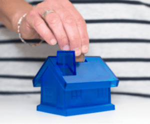 Save Money for a House 
Women deposits coins in a house-shaped piggy bank 