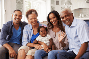 Family portrait of a black family with a mum, dad, grandparents and a baby sitting on a couch