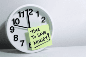 A white clock with a post-it attached it noted 'Time to Save Money!'